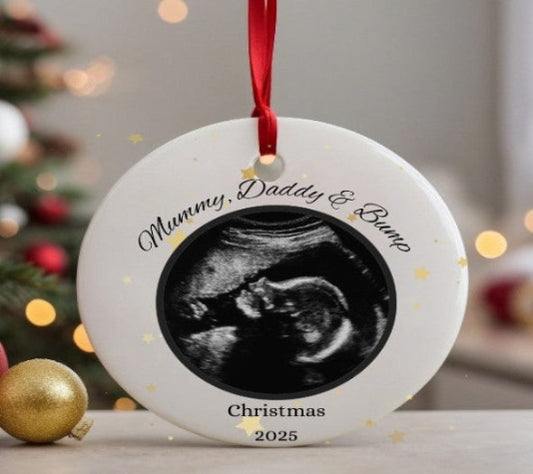 Decorative ornament with ultrasound photo and text 'Mummy, Daddy & Bump' in front of a Christmas tree.