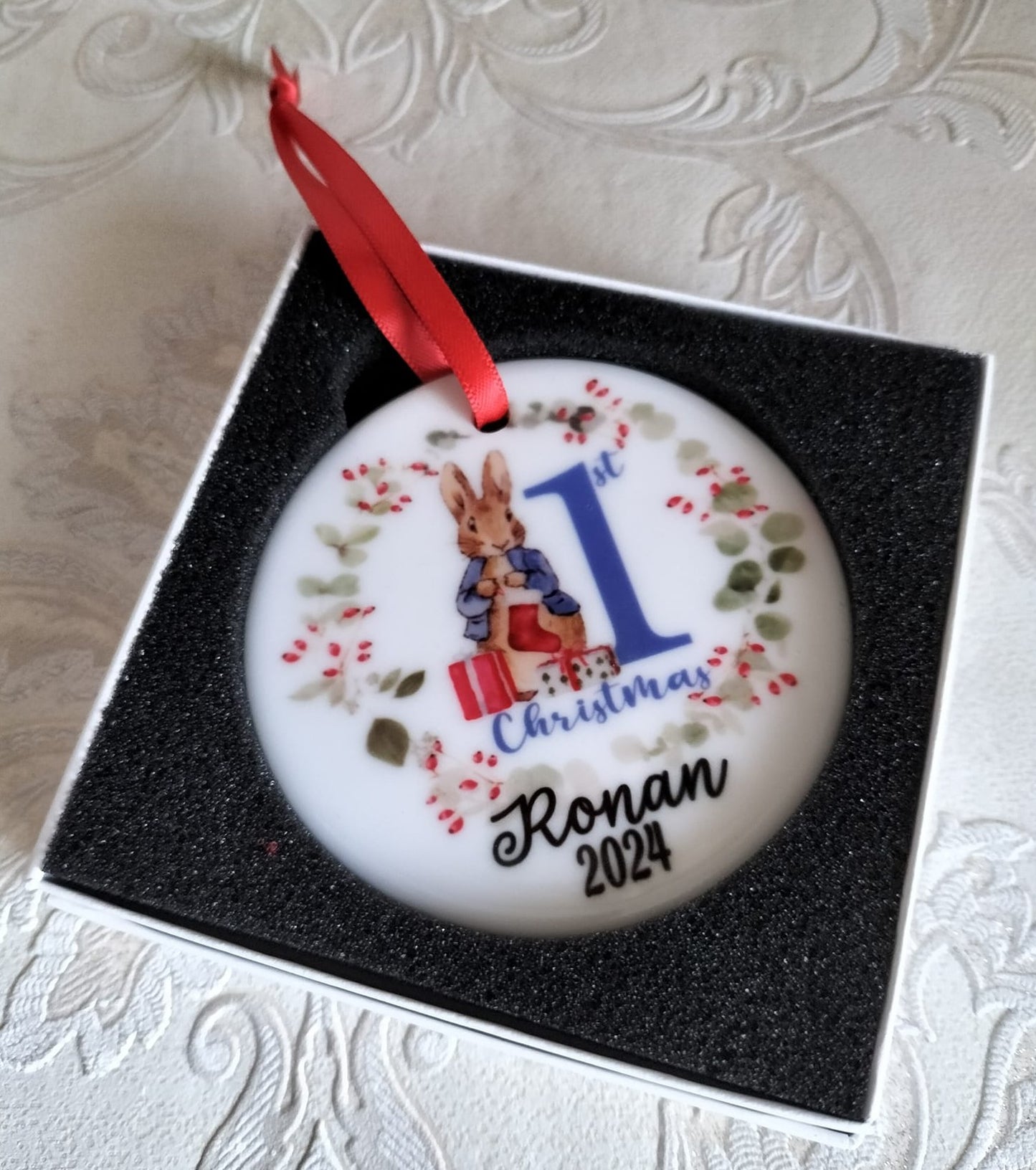 Personalised Christmas ornament with a red ribbon, featuring '1st Christmas Ronan 2025' on a white background.