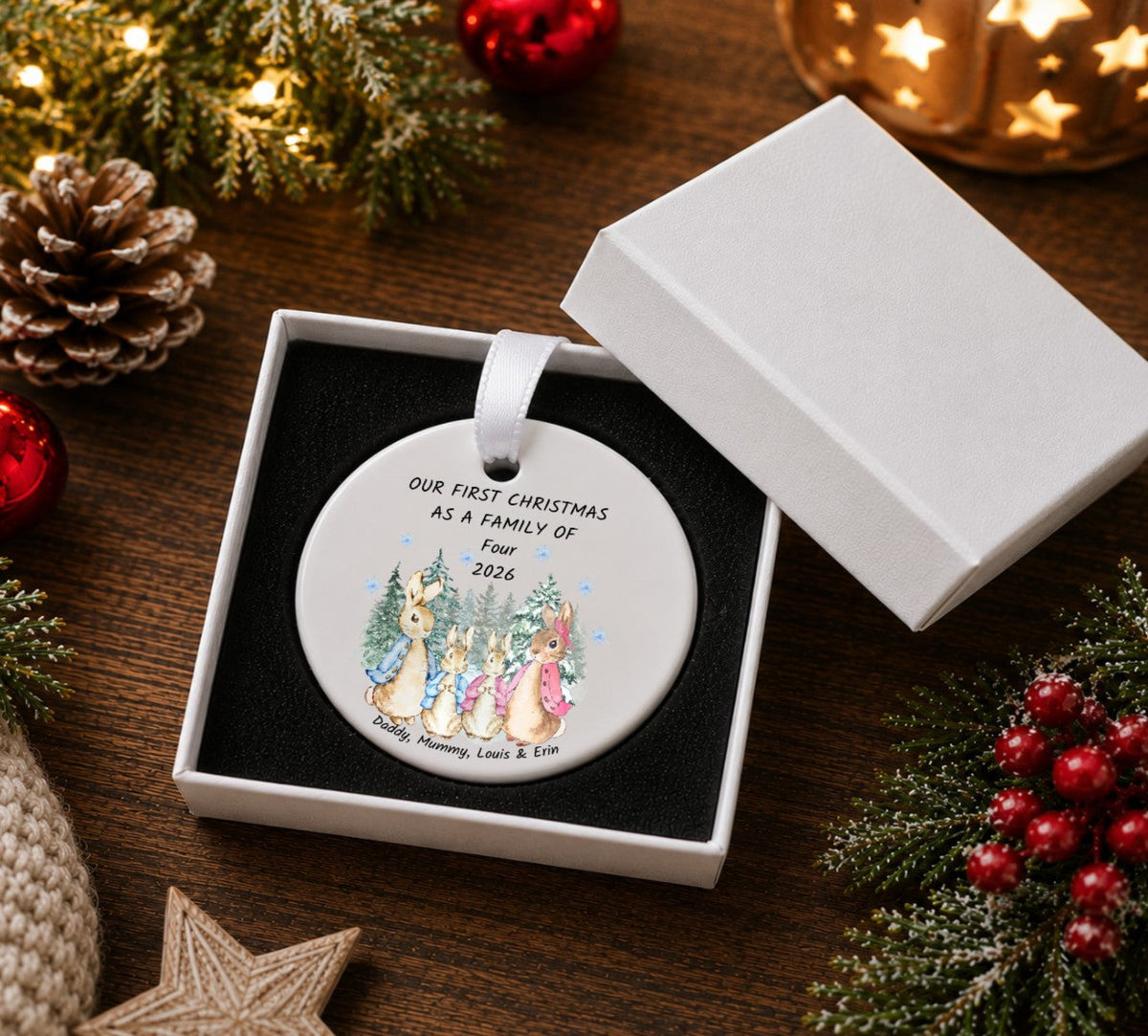 A round personalised Christmas ornament displayed in an open white gift box . The ornament features a white background with a printed illustration of four rabbits and the text 'OUR FIRST CHRISTMAS AS A FAMILY OF Four 2026'