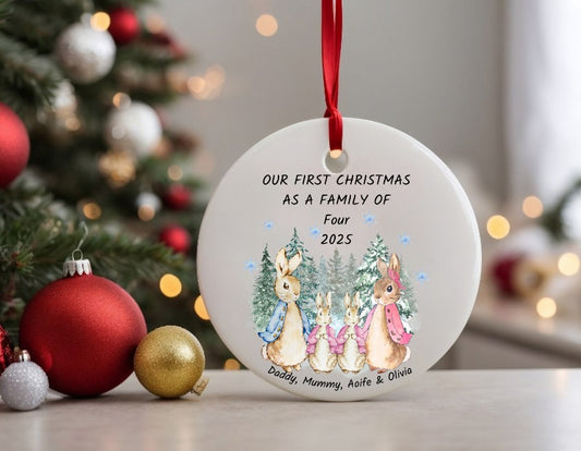 Personalised Christmas ornament with family illustration and text, placed in front of a decorated Christmas tree.