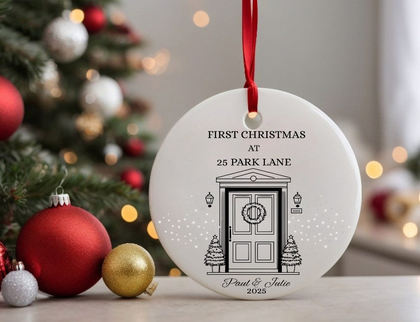 Christmas ornament with a door illustration and text, placed in front of a decorated Christmas tree.