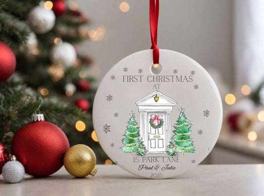 Personalised Christmas ornament with a house illustration and text, placed on a surface with festive decorations.