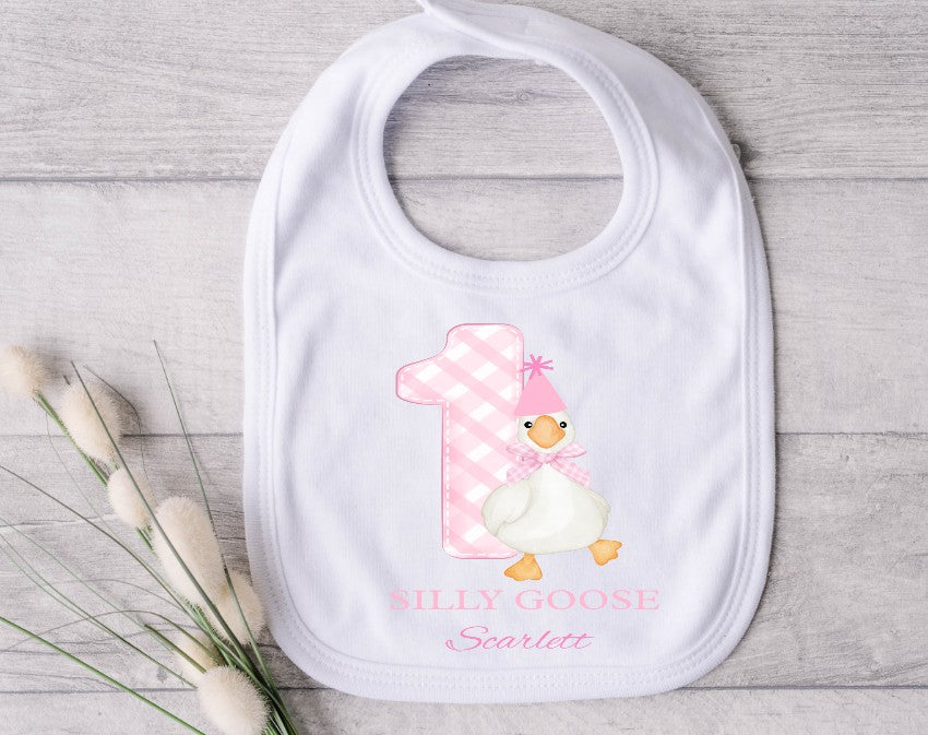 Baby bib with a cartoon goose design and text on a wooden surface