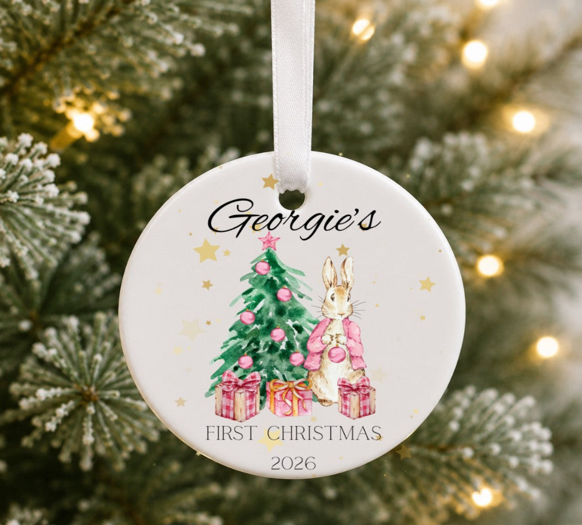 Christmas ornament hanging on a tree with illustration of a bunny wearing a pink jacket standing alongside a Christmas tree, personalised.