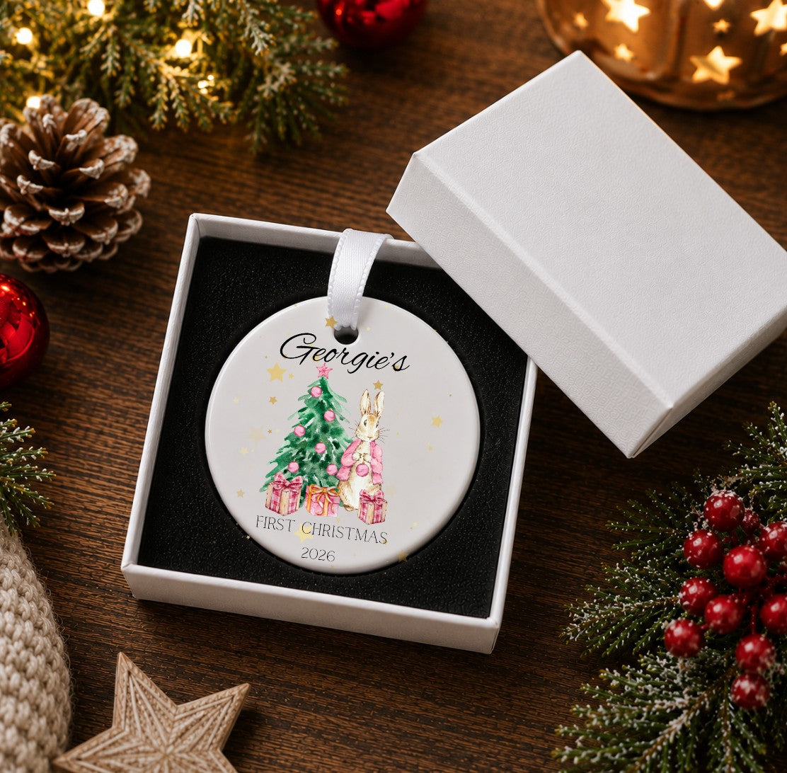 Christmas ornament in a white gift box with an illustration of a bunny wearing a pink jacket standing alongside a Christmas tree, personalised.