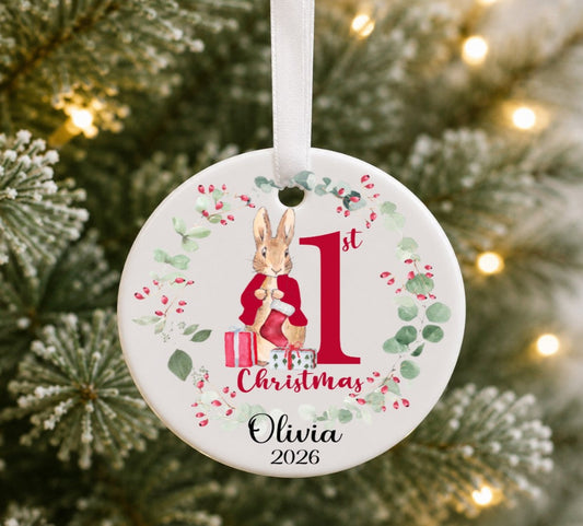 Ceramic round Christmas ornament hanging on a tree with an illustration of a rabbit wearing a red jacket, personalised with 1St Christmas Olivia 2026.
