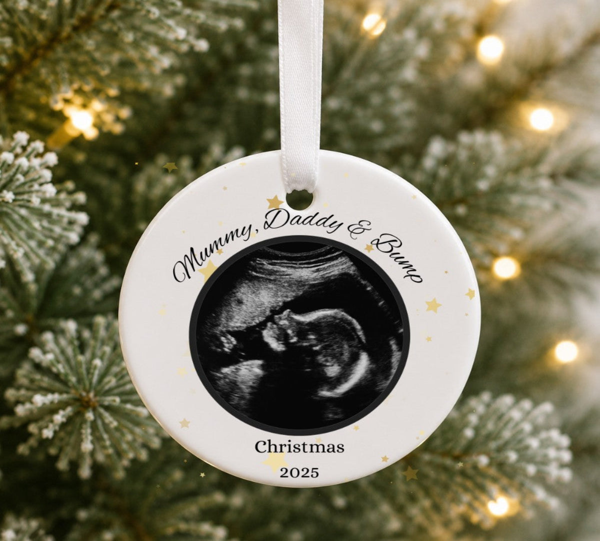A personalised round ceramic Christmas ornament displayed on a Christmas tree. The ornament features a black-and-white ultrasound photo in the centre with the custom text 'Mummy, Daddy & Bump' and 'Christmas 2026' printed on a white background.