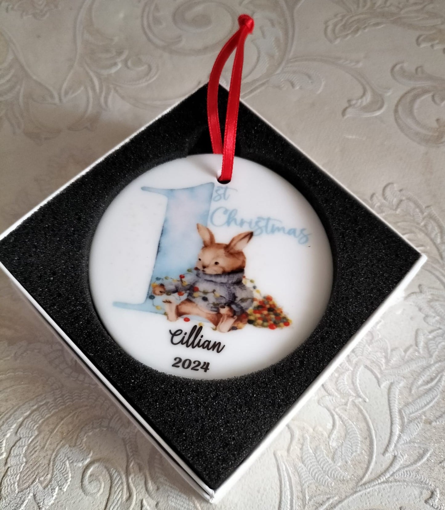 Round Christmas ornament with a rabbit design and text, placed in a box.