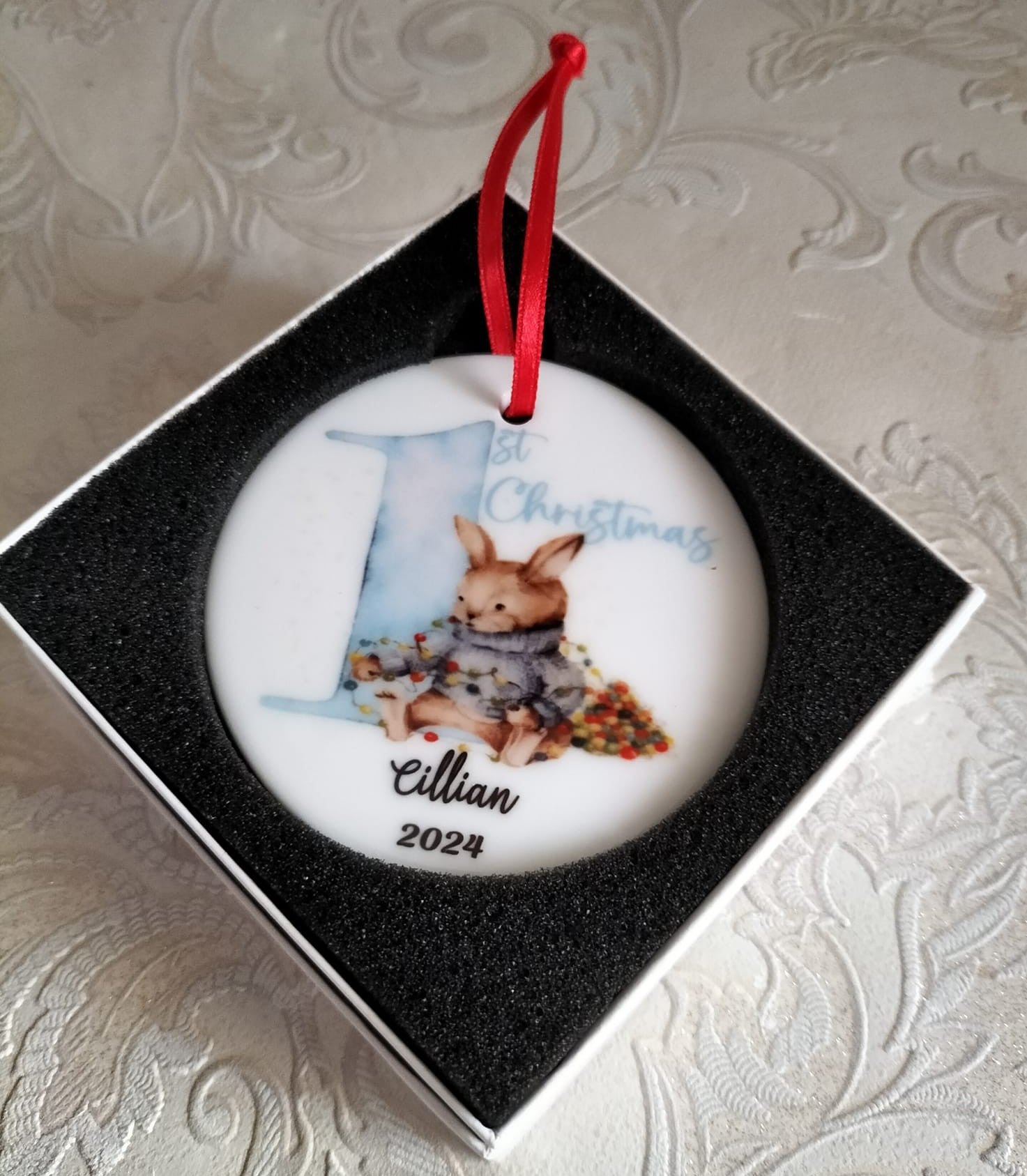 Round Christmas ornament with a rabbit design and text, placed in a box.