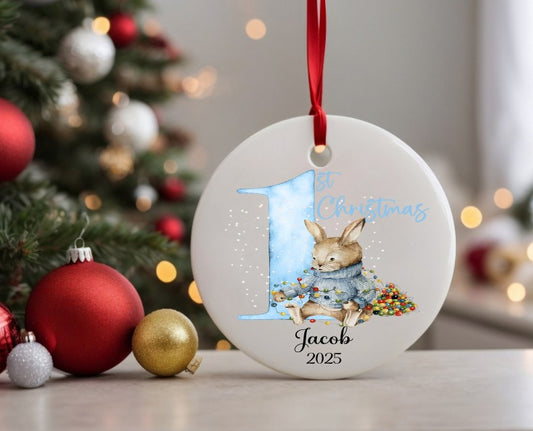 Personalised Christmas ornament with a rabbit and '1st Christmas' text, decorated tree in the background.