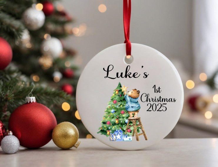 Personalised Christmas ornament with 'Luke's 1st Christmas 2025' text, decorated tree illustration, and red ribbon against a festive background.