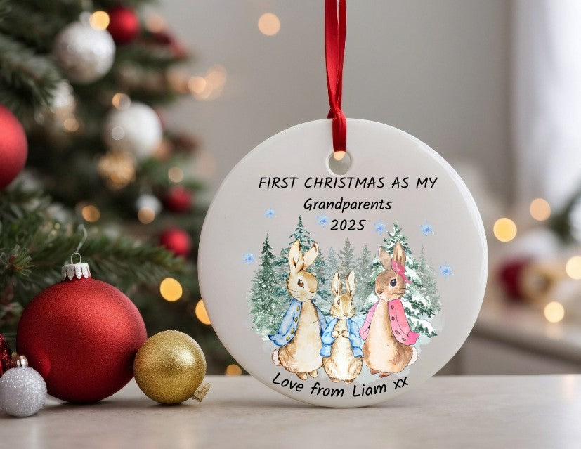 Decorative ornament with rabbits and text 'First Christmas as my Grandparents 2025' in front of a Christmas tree.