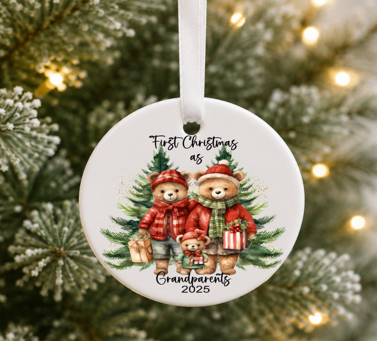 A round white ceramic Christmas ornament hanging from a white ribbon, featuring an illustration of three teddy bears in red and green holiday clothing with pine trees and the text 'First Christmas as Grandparents 2025'. The ornament is photographed against a blurred Christmas tree background with warm string lights.