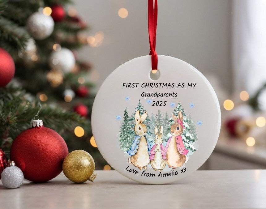 Christmas ornament with rabbits and text 'First Christmas as my Grandparents 2023' in front of a decorated tree.