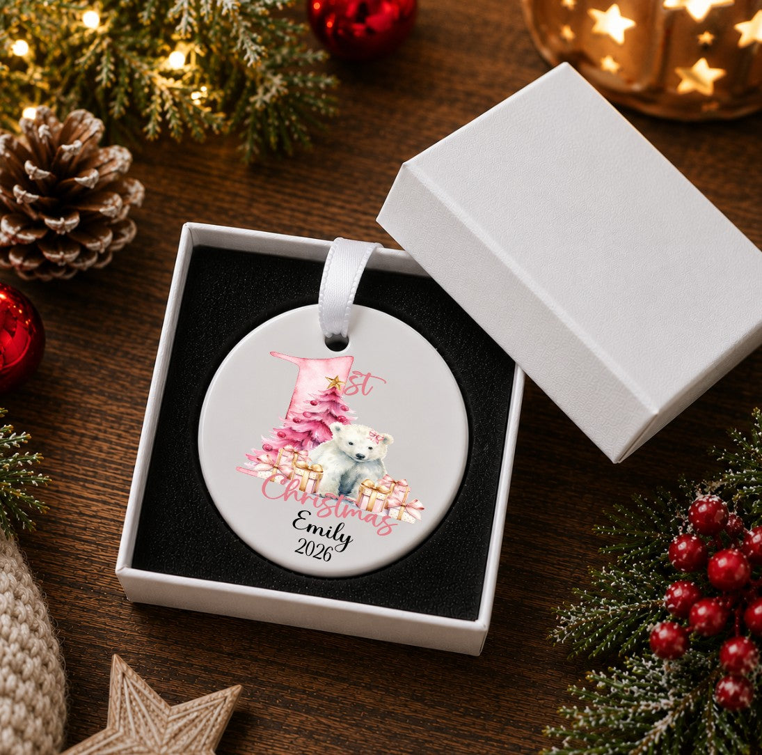 A round personalized Christmas ornament displayed in an open white gift box. The ornament features a white background with an illustration of a white dog in a pink stocking and the text 'Best Christmas Emily 2026'.