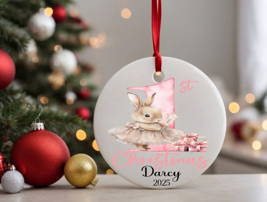 Christmas ornament with a bunny design and text, placed in front of a decorated Christmas tree.