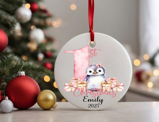 Christmas ornament with penguin and gift design, featuring '1st Christmas Emily 2025' text, against a festive background.